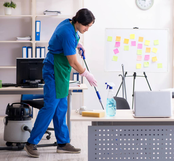 Die männliche hübsche professionelle Reinigungskraft bei der Arbeit im Büro - Foto, Bild