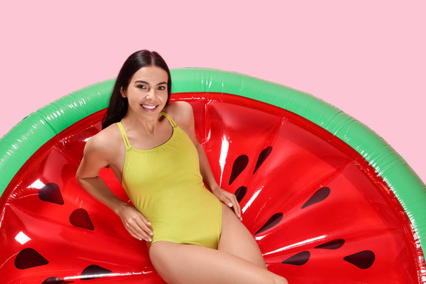 Young woman wearing stylish swimsuit on inflatable mattress against pink background - Фото, зображення