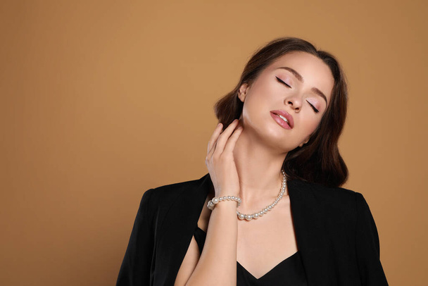 Young woman wearing elegant pearl jewelry on brown background, space for text - Fotoğraf, Görsel