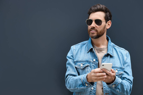 Handsome bearded man with smartphone near grey wall outdoors. Space for text - Φωτογραφία, εικόνα