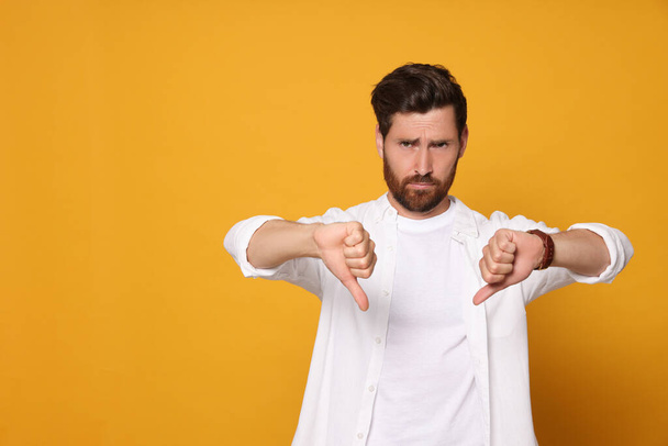 Handsome bearded man showing thumbs down on orange background. Space for text - Foto, Imagem