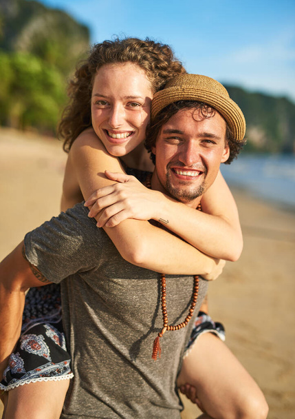 The tans may fade but the memories will last forever. Portrait of a happy young man giving his girlfriend a piggyback ride on the beach - Photo, Image