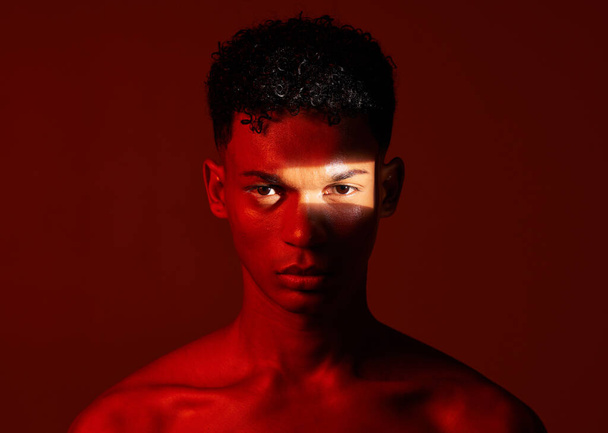 Szépség, vörös stúdió és portré egy férfiról, akinek fénysugár van az arcán, bőrápoló gyakorlattal. Egészség, reflektorfény és modell, barna háttérrel izolált wellness bőrkezeléssel - Fotó, kép