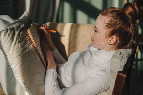 Schöne junge Frau entspannt auf dem Sofa mit Gesichtsmaske Behandlung Lesen Buch zu Hause. Menschen Alltag für Hauterkrankungen Lebensstil zu Hause - Foto, Bild