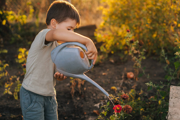Entzückender kleiner Junge, der Pflanzen mit der Gießkanne im Garten gießt, den Eltern hilft, die Pflanzen zu pflegen und Spaß hat. Aktivitäten mit Kindern im Freien. - Foto, Bild