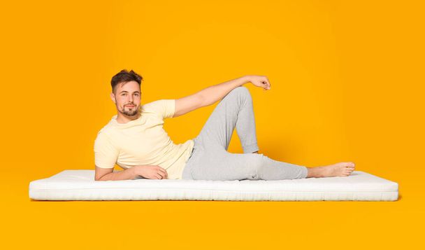 Man lying on soft mattress against orange background - Photo, image