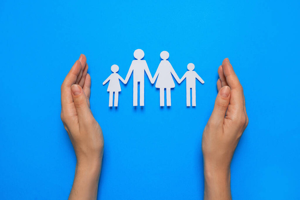 Woman protecting paper family cutout on light blue background, top view. Insurance concept - Foto, imagen