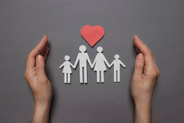 Woman protecting paper family figures and red heart on grey background, top view. Insurance concept - Foto, immagini