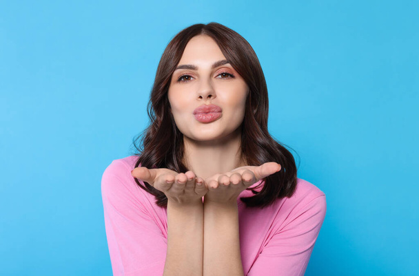 Beautiful young woman blowing kiss on light blue background - Photo, Image