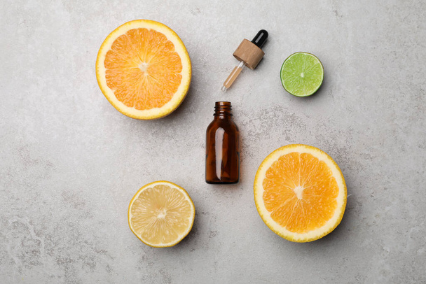 Bottle of citrus essential oil and fresh fruits on light table, flat lay - Фото, изображение