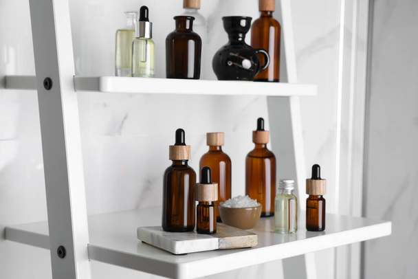 Essential oils, sea salt, and other cosmetic products on white shelving unit in bathroom - Фото, зображення