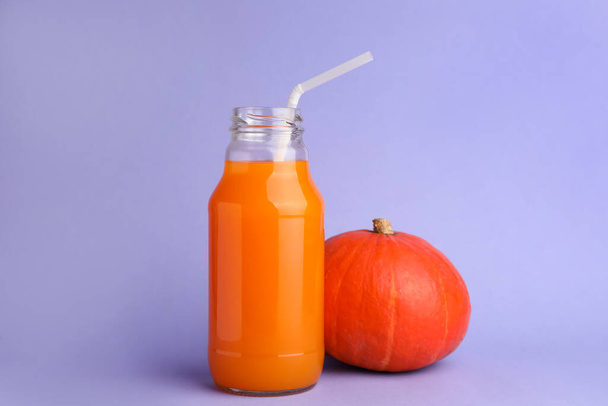 Tasty pumpkin juice in glass bottle and whole pumpkin on lavender color background - Photo, Image