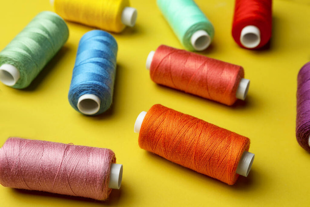 Different colorful sewing threads on yellow background - Foto, imagen