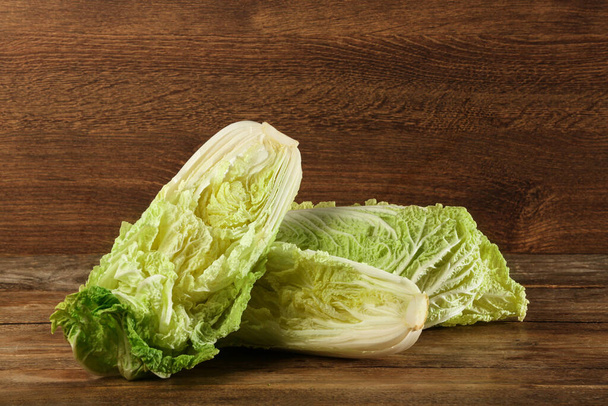 Cut fresh ripe Chinese cabbage on wooden table - Фото, изображение