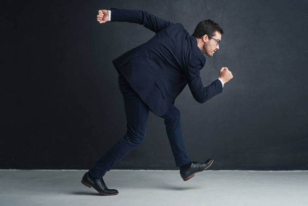 Running the corporate rat race. Studio shot of a businessman running against a gray background - Φωτογραφία, εικόνα