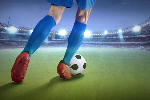 Rear view of a football player man in a blue jersey kicking the ball on the football field - Φωτογραφία, εικόνα