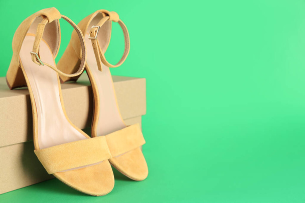Cardboard box with yellow heeled sandals on green background - Foto, Imagen