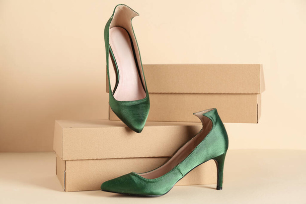 Cardboard boxes with green high-heeled shoes on beige background - Photo, Image