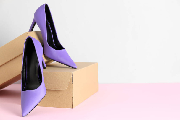 Картонные коробки с фиолетовыми туфлями на высоком каблуке на столе возле белой стены - Фото, изображение