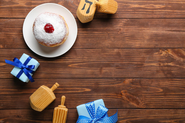 Marco hecho de plato con sabroso donut, dreidels y regalos para la celebración de Hanukkah sobre fondo de madera - Foto, imagen