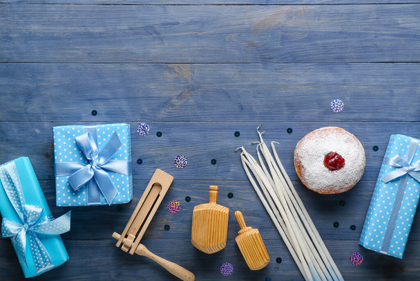 Tasty doughnut with dreidels, candles, rattle and gifts for Hannukah celebration on blue wooden background - Photo, Image