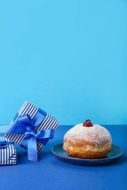Assiette avec beignet savoureux et cadeaux pour la célébration Hannukah sur fond bleu - Photo, image
