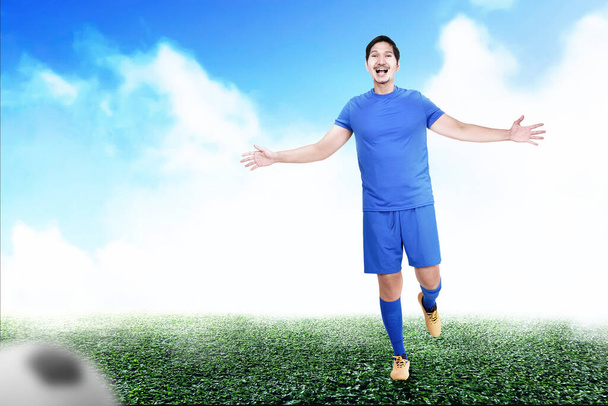 Asian football player man in a blue jersey celebrates the victory on the football field - Foto, imagen