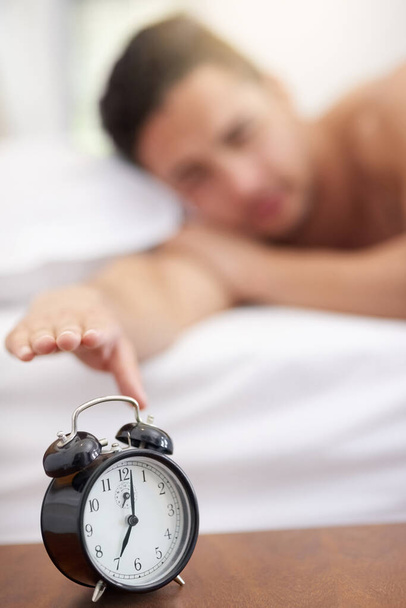 Dit is je wekdienst van zeven uur. een jonge man reikt naar zijn wekker in de ochtend - Foto, afbeelding