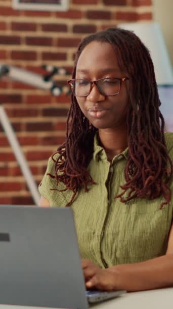 Vidéo verticale : Afro-Américaine utilisant un ordinateur portable et faisant un travail à distance à la maison, travaillant sur freelance avec des informations sur l'entreprise et le rapport. Créer un e-mail financier à envoyer au gestionnaire, apprendre les ventes. - Séquence, vidéo