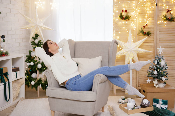 幸せな女性リラックス上のアームチェアで装飾されたクリスマスルーム - 写真・画像