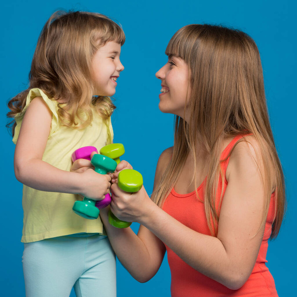 mamá y su hija en el entrenamiento de fitness, primer plano, emociones y gestos, concepto, sobre fondo azul - Foto, Imagen