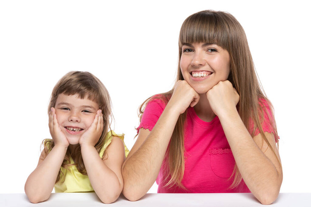 mom and her little daughter sitting at the table laughing, happy family, on a white background, isolate - Photo, Image