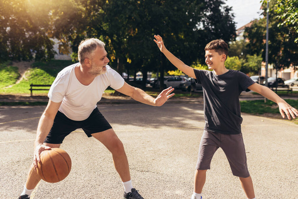 Зрілий чоловік грає в баскетбол з сином
 - Фото, зображення