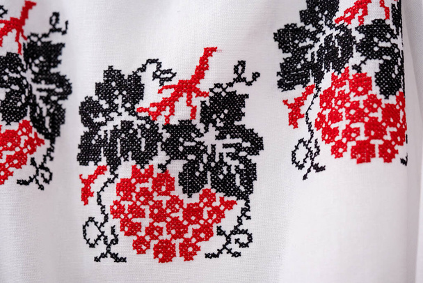 Vyshyvanka - Ukrainian national outfit. Cross stitch in red, black and white. Close up pattern of vyshyvanka blouses with grapes. Blur and selective focus - Photo, Image