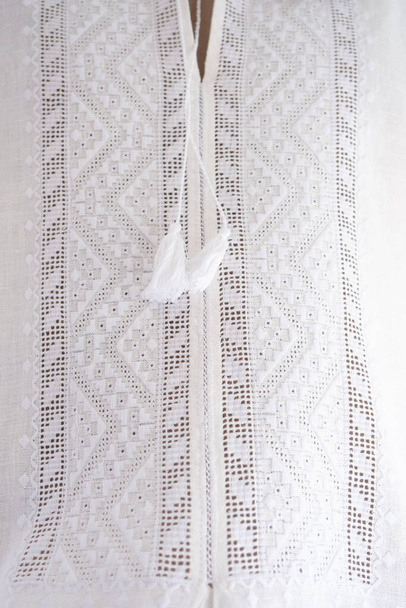 Vyshyvanka - Oekraïense nationale jurk. Herenhemd, borduurwerk met witte draden op witte, wazige en selectieve focus. Talisman, handgemaakte kruissteek, geometrisch ornament, Oekraïense cultuur - Foto, afbeelding