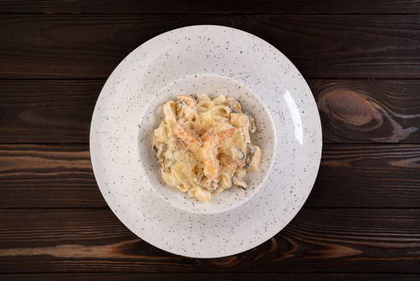 Italské těstoviny fettuccine s krevetami a mušlemi v krémové omáčce s parmezánem na talíři na dřevěném stole. horní pohled, kopírovací prostor - Fotografie, Obrázek