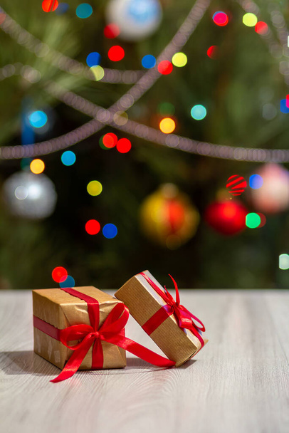 赤い弓でギフトボックス。背景にキラキラとぼやけたパーティーライトとおもちゃのボールを持つクリスマスツリー。クリスマスのお祝い. - 写真・画像