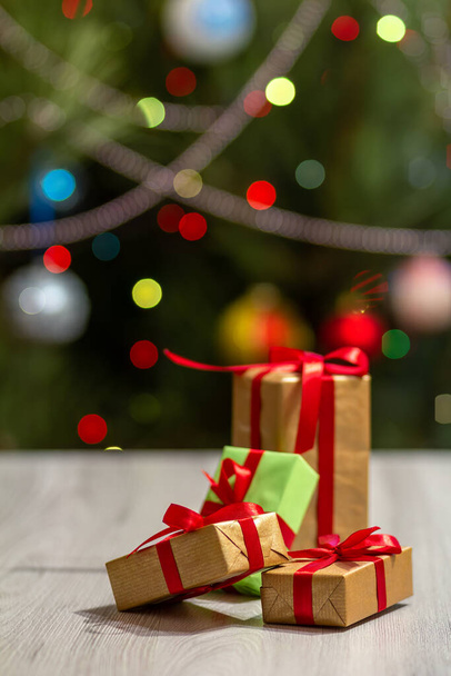 Gift boxes with red bows. Christmas tree with blurred twinkling party lights and toy balls on the background. Christmastime celebration. - Foto, Imagen