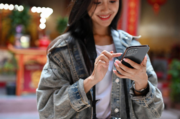 Vista de cerca de una mujer joven sosteniendo un teléfono inteligente mientras viaja en el templo tradicional asiático - Foto, Imagen