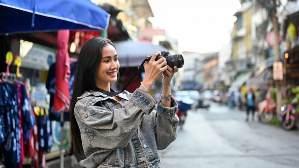 Jeune femme gaie prenant une photo des produits locaux tout en voyageant dans le marché local asiatique  - Photo, image