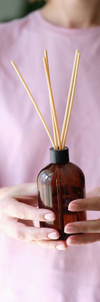 Close-up of woman holding aroma reed diffuser, home fragrance bottle with rattan sticks and smell of freshness - Photo, image