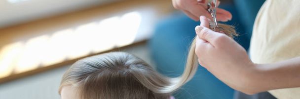 Top view of hairdresser making stylish hairstyle to cute little girl. Haircutter cuts and styles hair of small child. Fashion concept - Fotoğraf, Görsel