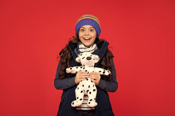 surprised child in puffer jacket hold toy. teen girl on red background. happy childhood. kid playing toy. - Foto, immagini