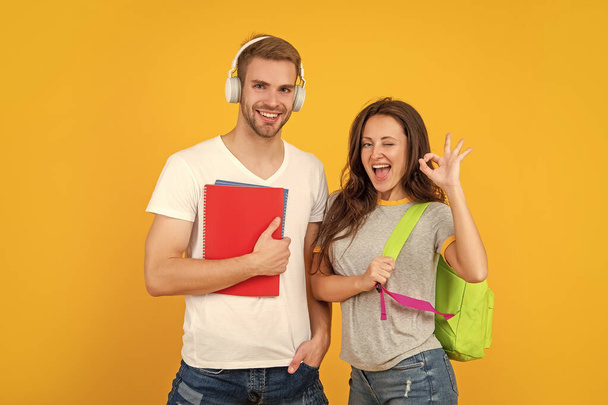 modern education. knowledge day. guy and girl hold notebook. university students on yellow background. study with workbook. ok. cheerful couple in headphones and backpack. back to school. - Φωτογραφία, εικόνα