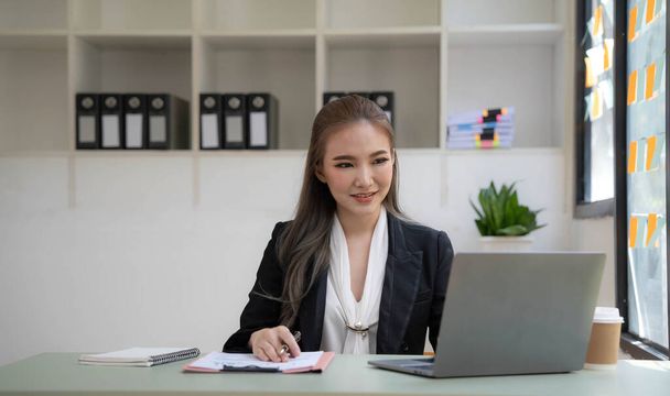 Egy fiatal nő egy laptopon dolgozik az irodában. Ázsiai üzletasszony ül a munkahelyén az irodában. Beautiful Freelancer Woman online dolgozik otthonában - Fotó, kép