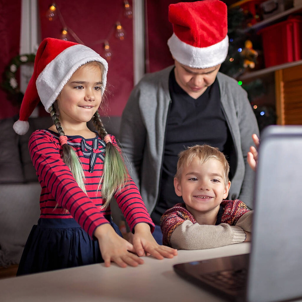 Turvallinen online joulujuhla. Onnellinen perhe Santa punainen hatut juhlii ystävien kanssa lähes internetin kautta ja kannettavan. Videopuhelu. Jää kotiin, kaukainen loma, elämäntapa - Valokuva, kuva