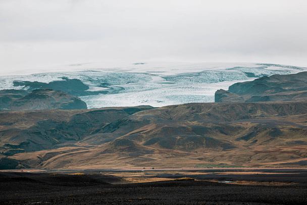 Fekete vulkanikus homokos strandok Izlandon, kilátás a szárazföld felé, folyó vályú és néhány sárga lombozat a víz körül.  - Fotó, kép