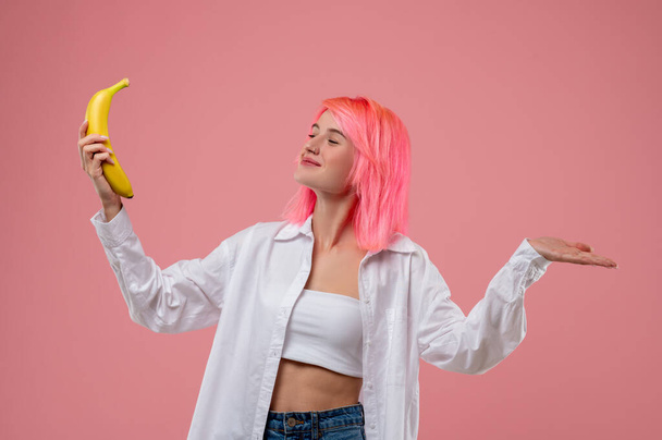 Smiling happy cute girl with a nose ring posing for the camera with the yellow banana in the lifted hand - Photo, image