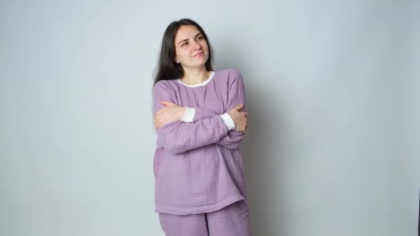 Een brunette vrouw in paarse warme mousseline pyjama knuffelt zichzelf en geniet van het comfort van slapende kleren. - Video