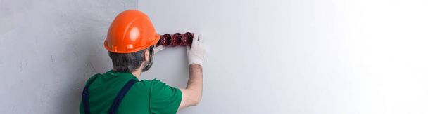 Um eletricista instala tomadas no apartamento. Um cara com um capacete laranja e macacão faz elétrica na casa. - Foto, Imagem